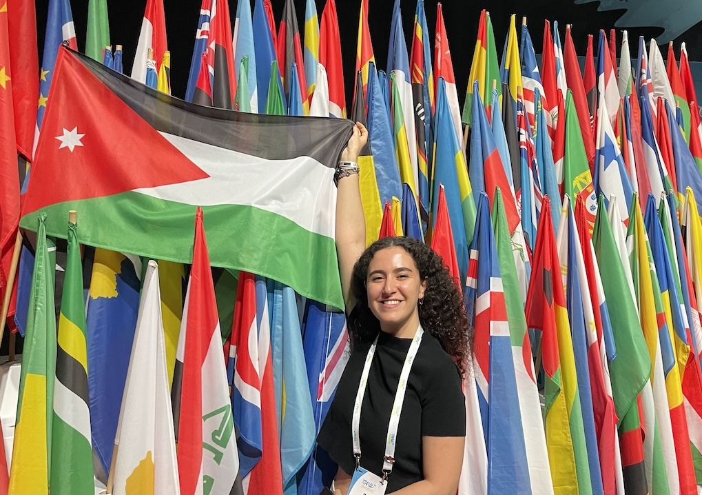 Maya Zabaneg standing in front of the flags of the world